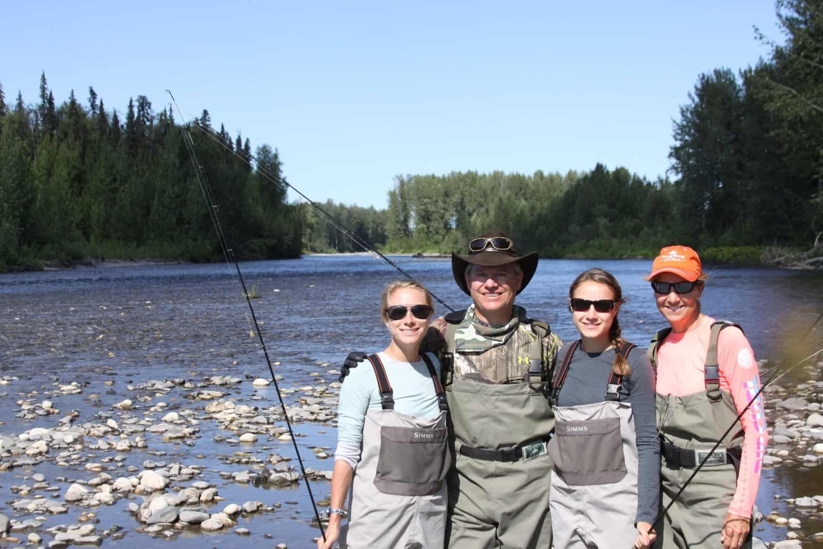Alaska fishing lodge family fishing by the river in sunny weather at Wilderness Place Lodge.